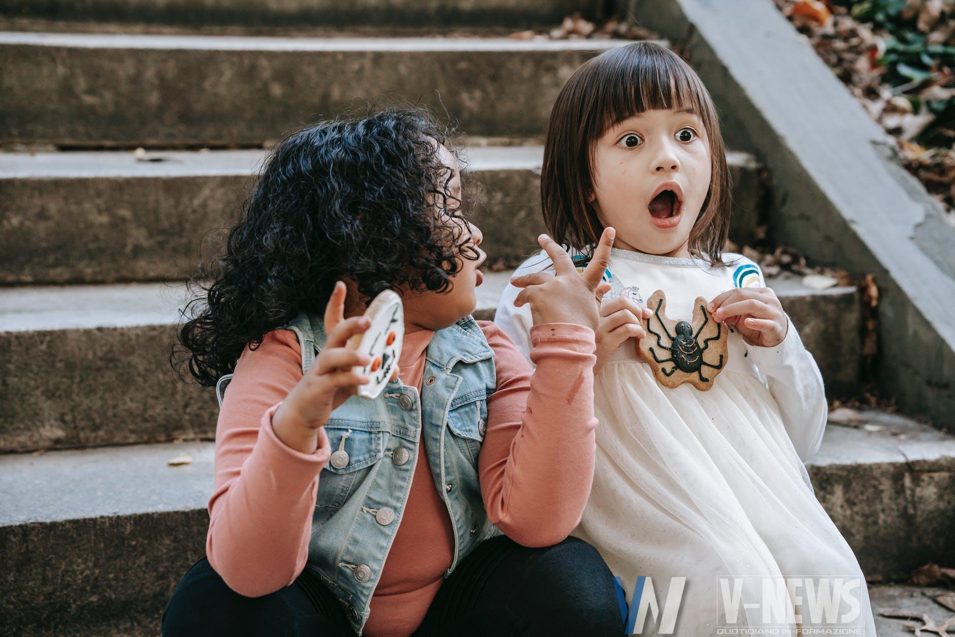 amazed diverse girls with halloween gingerbread cookies sitting on staircase