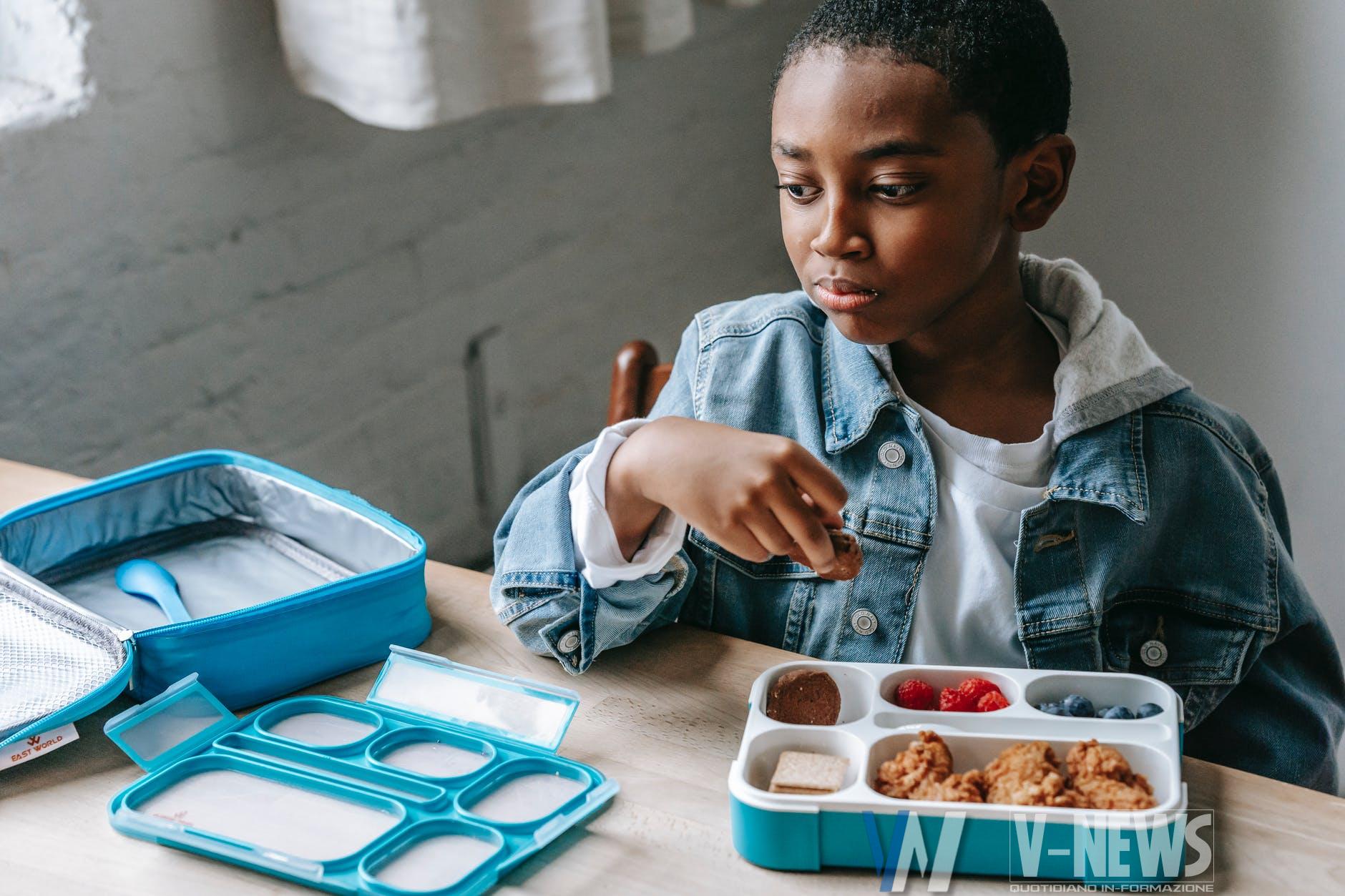 crop dreamy black schoolboy with lunch box in classroom