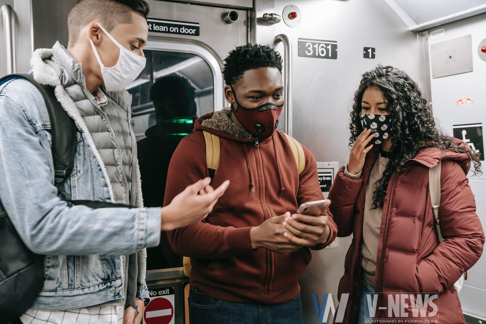 faceless multiethnic students in masks in subway train with phone